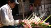 A man attaches pink flowers and broad folded leaves onto the frame of a cross